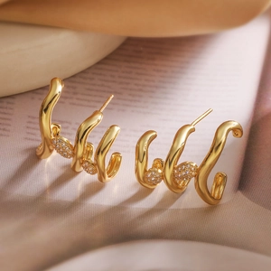 Boucles d'oreilles vagues plaquées or avec zircons cubiques posées sur un tissu soyeux