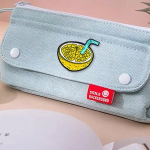 Creative enamel pin featuring a yellow lemon brain design with blue straw on canvas bag