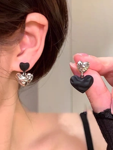 Detail showing asymmetric black and silver liquid metal heart earrings on model and hand