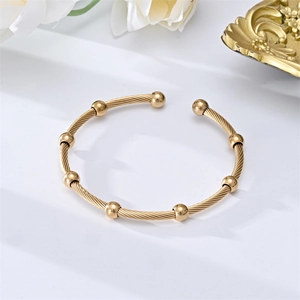 Detailed shot of golden cable wire bangle with eight polished beads on a minimal desk