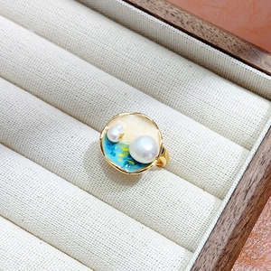 Vue macro d'une bague dorée avec émail bleu et blanc et perles naturelles