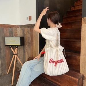 Detail of striped canvas tote bag with red Bonjour embroidery on a wooden staircase