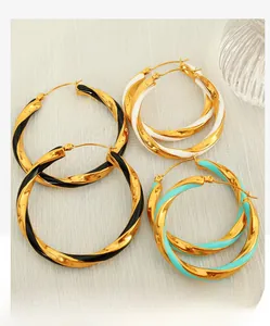 Detailed view of large gold twisted hoop earrings with black, white and turquoise enamel