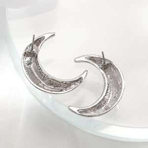 Detailed close-up of crescent moon earrings with unique hammered texture on silver metal