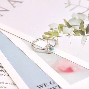 Detailed close-up of a silver ring with moon motif and turquoise bead on open book
