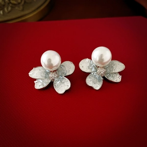 Detailed close-up of floral stud earrings with large pearl centers on red background