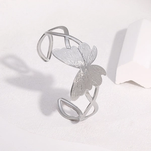 Detail of silver butterfly open bangle with textured wings on a white minimalist display