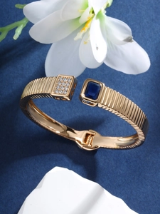Close-up of golden bangle featuring blue rectangular gemstone and sparkling crystal details