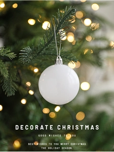 Glossy white Christmas ball ornament hanging on a green tree with warm bokeh lighting