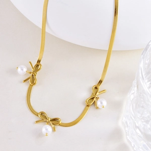 Detailed close-up of golden flat snake chain with bow charms and white pearls