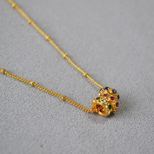 Détail macro du collier en laiton plaqué or avec pendentif évidé et zircons colorés