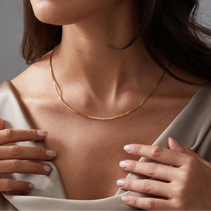 Close-up of a sleek golden box chain necklace worn over champagne silk fabric
