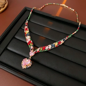 Close-up of golden necklace featuring colorful rectangular stones and pink heart pendant