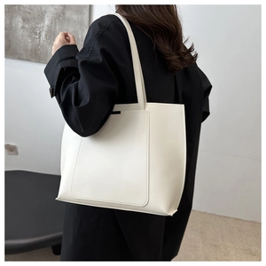 Model wearing a minimalist cream PU leather tote bag over a black winter coat