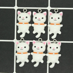 Close-up of white cat charms with orange collars and metal rings for DIY jewelry