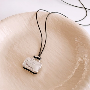Detailed close-up of a silver handbag charm with engraved logo on a black cord necklace