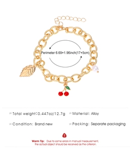 Dettaglio di foglia dorata, ciliegia rossa e ciondoli di perle su un bracciale a maglie