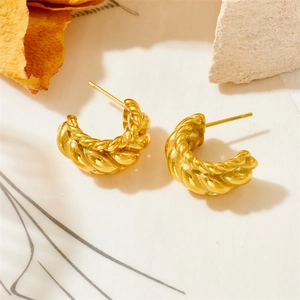 Detail shot of golden twisted C-shaped earrings with matte finish on textured stone