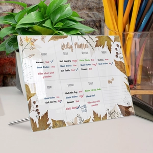 Clear acrylic weekly planner with autumn leaf design and printed schedule on an office desk