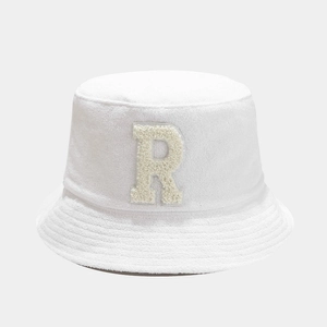 Close-up of white bucket hat featuring a textured fuzzy R letter patch in beige bouclé
