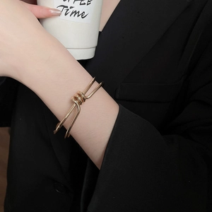 Close-up of golden dual-line twisted metal cuff bracelet on a black suit sleeve