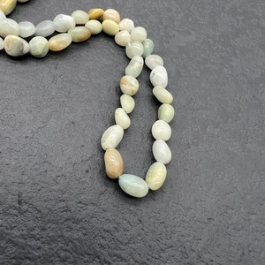 Macro shot of natural irregular stone beads in pastel green and white on dark slate