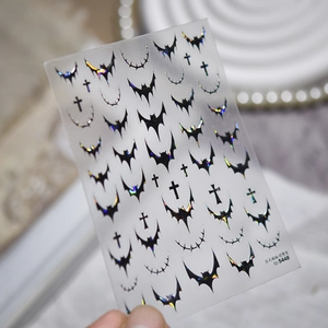 Detail of gothic metal nail stickers with iridescent bat and moon patterns on marble base