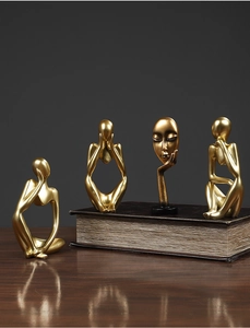 Close-up of four golden abstract thinker resin sculptures on vintage books with reflections