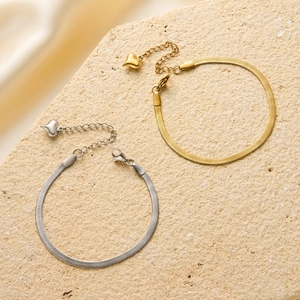 Detail of gold and silver snake chain bracelets with heart charms on stone background