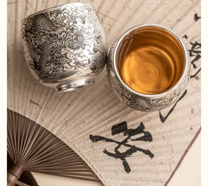 Détail de tasses à thé en argent avec gravures de dragon sur une table en bois