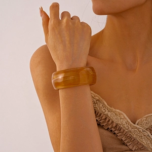 Close-up of wide amber acrylic bangle with natural marble texture on model wrist