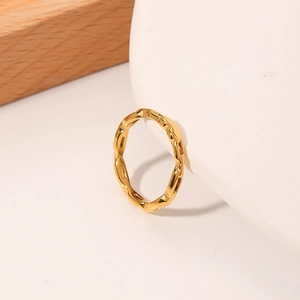 Minimalist 18K gold wave pattern titanium steel ring on a minimalist white display base