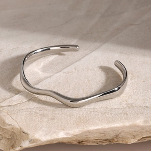 Macro detail of wavy silver open cuff bracelet on a natural stone background