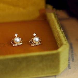 Elegant gold crown pearl earrings with sparkling zircons on green velvet background