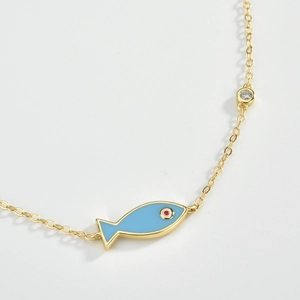Macro detail of gold fish pendant with blue enamel and sparkling white zircon accent