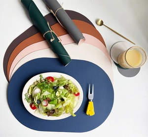 Flat lay of oval faux leather placemats and coasters in assorted colors with tableware