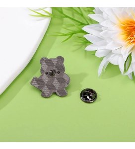 Detailed view of a dark grey bear enamel pin with butterfly clutch back on green surface
