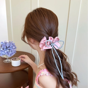 Pink checkered bow hair accessory styled on a low ponytail in a cozy cafe setting