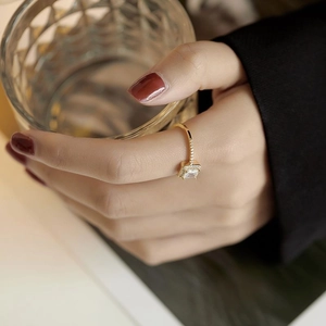 Detail of square zircon ring in gold with side stones worn by a model holding glass