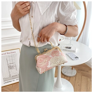 Detail of pink floral embroidery handbag with gold kiss lock and chain held by a model