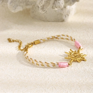 Détail du bracelet pendentif soleil avec corde tissée rose et blanc et chaîne dorée