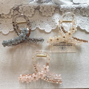 Detailed view of three crystal flower hair claws in grey-blue, beige, and pink shades
