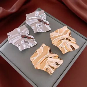 Irregular textured square gold and silver metal earrings on luxury jewelry box display