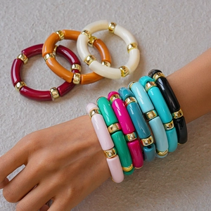 Dettaglio di braccialetti in acrilico colorato con distanziatori dorati su fondo strutturato