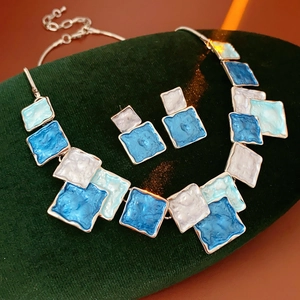Close-up of geometric blue enamel necklace and square stud earring set on velvet