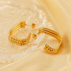 Detailed close-up of golden rectangular earrings with a twisted woven texture design