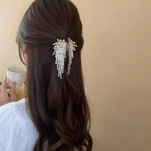 Detailed view of the faux pearl tassel hair claw with elegant beads on white knit sweater