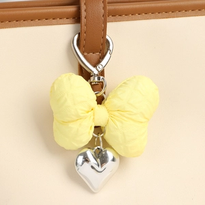 Close-up of yellow quilted bow pendant with silver heart charm on leather strap