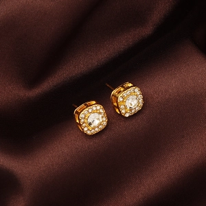 Close-up of gold square stud earrings with zircon inlay on brown silk fabric background