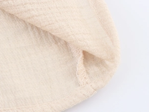 Detailed close-up of beige cotton linen fabric showing intricate embroidery and seam texture